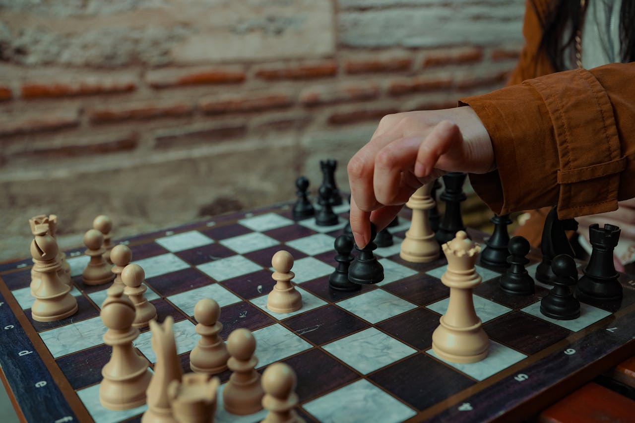 home-hero-bg A person making a chess move on a wooden board with brick wall background.